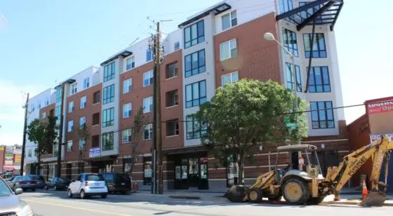 A modern apartment complex with a busy street with cars and construction vehicles