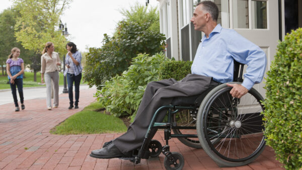 Man with spinal cord injury in a wheelchair coming out of a door onto the street